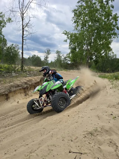 Zielony quad w zakręcie, spod kół sypie się piach