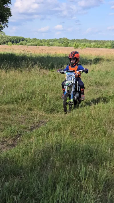 Dziecko na motocyklu crossowym jedzie ścieżką przez łąkę