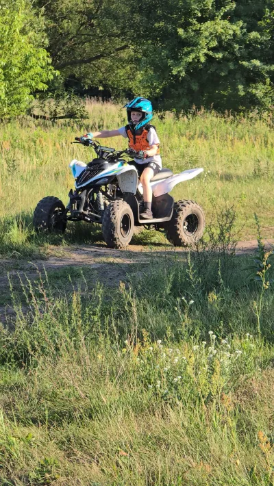 Dziecko w niebieskim kasku na quadzie na trawiastej ścieżce